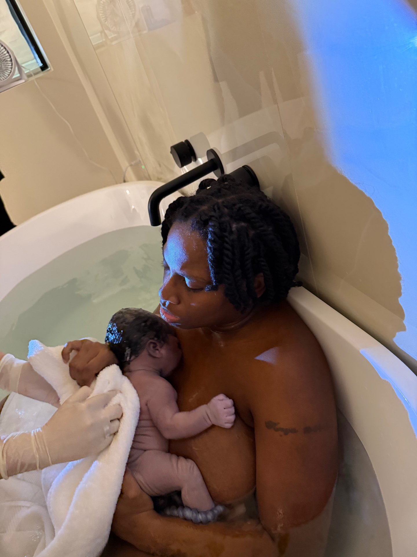 A mother cradles her newborn skin to skin in a warm birth tub