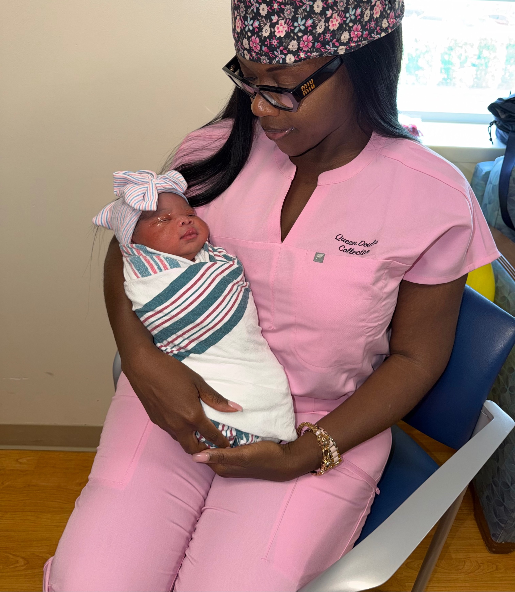 Tamarah of Queen Doula Collective gently holding a newborn in pink scrubs
